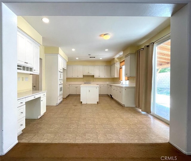 kitchen featuring a center island, light countertops, white cabinetry, and white oven