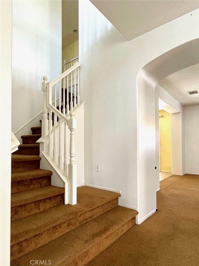 stairs with arched walkways, carpet flooring, baseboards, and visible vents