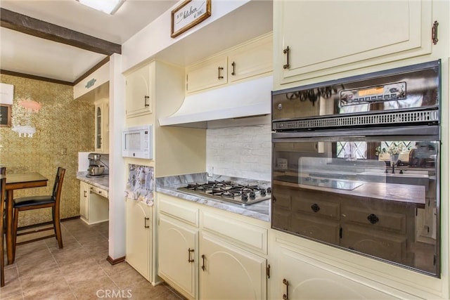 kitchen featuring white microwave, stainless steel gas cooktop, backsplash, and cream cabinetry