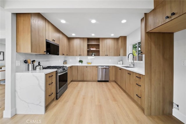 kitchen with open shelves, modern cabinets, light wood-type flooring, a sink, and stainless steel appliances
