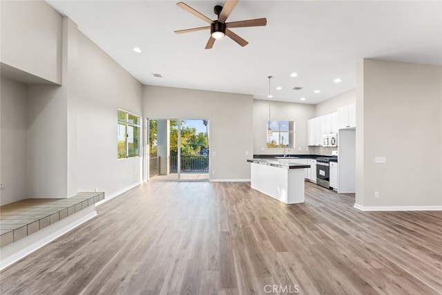 unfurnished living room featuring baseboards, recessed lighting, ceiling fan, light wood finished floors, and a sink