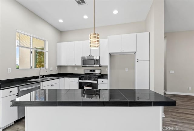 kitchen with dark wood-type flooring, white cabinets, dark countertops, a sink, and stainless steel appliances
