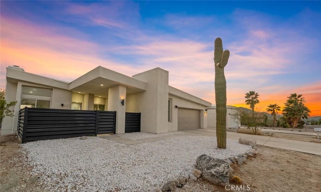contemporary house with driveway, stucco siding, fence, and an attached garage