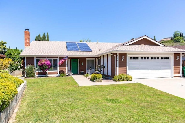 ranch-style house with roof mounted solar panels, a front yard, a chimney, a garage, and driveway