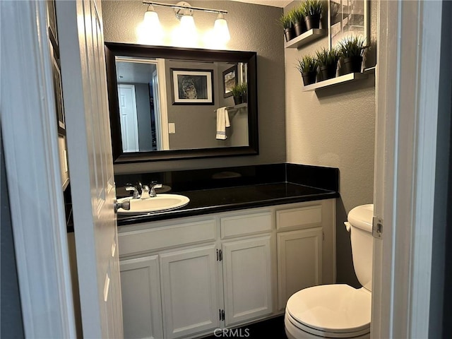 half bath featuring toilet, vanity, and a textured wall