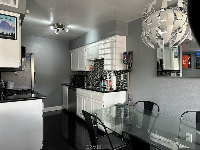 kitchen featuring white cabinets, dishwasher, backsplash, and dark countertops