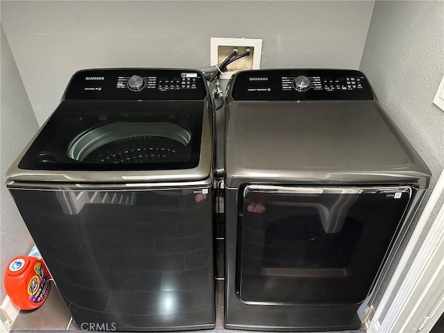 clothes washing area with independent washer and dryer, laundry area, and a textured wall