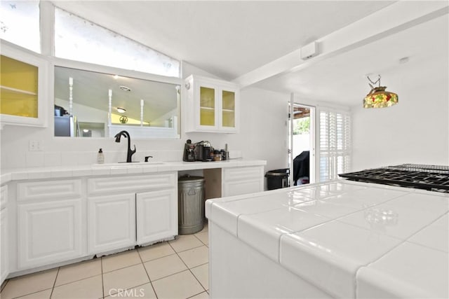 kitchen featuring a sink, glass insert cabinets, tile countertops, and light tile patterned floors