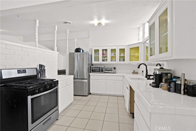 kitchen with tile counters, light tile patterned floors, white cabinets, stainless steel appliances, and a sink