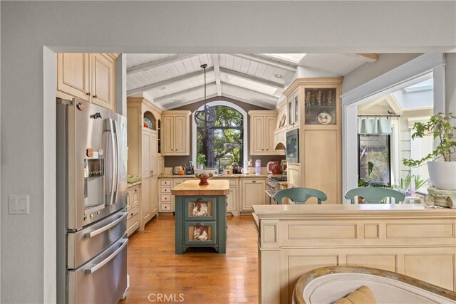 kitchen featuring light wood finished floors, stainless steel appliances, vaulted ceiling with beams, a center island, and butcher block counters