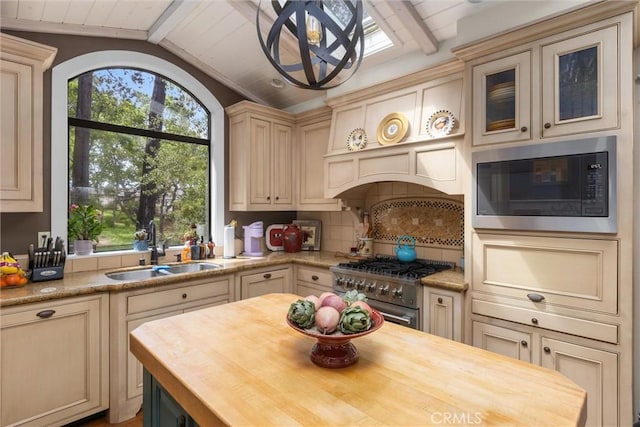 kitchen with built in microwave, a sink, cream cabinetry, vaulted ceiling with beams, and butcher block counters