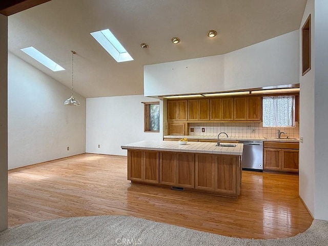 kitchen with tile countertops, stainless steel dishwasher, light wood-style flooring, a skylight, and a sink