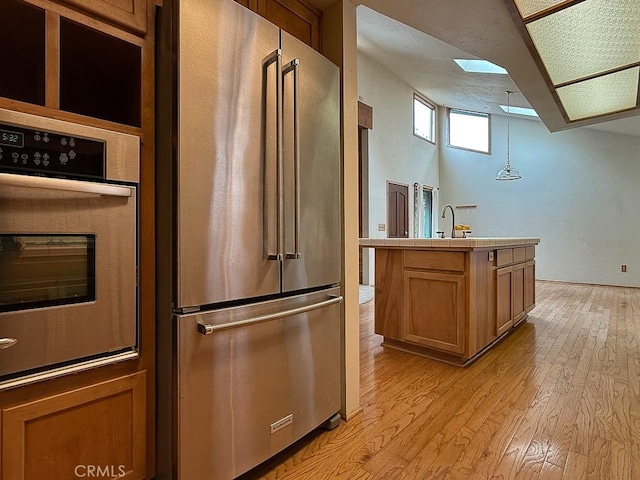 kitchen featuring a sink, light wood-style floors, brown cabinets, tile counters, and stainless steel appliances