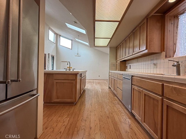 kitchen with light wood-style flooring, brown cabinets, decorative backsplash, tile countertops, and appliances with stainless steel finishes