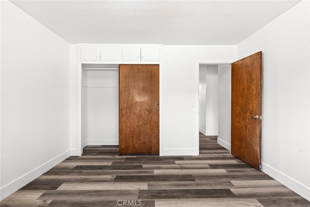 unfurnished bedroom with baseboards, dark wood-style floors, and a closet