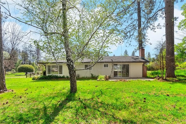 rear view of property with a lawn, a patio, a chimney, and stucco siding