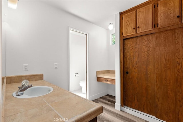 bathroom featuring a baseboard heating unit, wood finished floors, toilet, and a sink