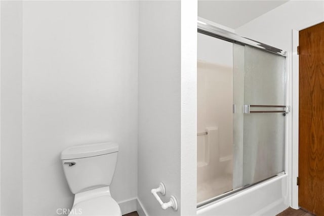 bathroom featuring baseboards, bath / shower combo with glass door, and toilet