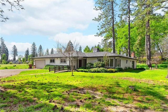 ranch-style home featuring a front yard, an attached garage, a chimney, and driveway