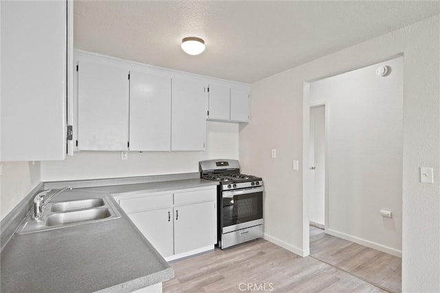 kitchen featuring white cabinets, gas stove, a sink, light wood finished floors, and baseboards