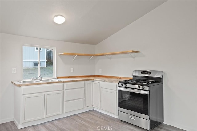 kitchen with light wood-style flooring, open shelves, white cabinets, a sink, and stainless steel gas range oven