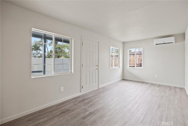 empty room featuring baseboards, wood finished floors, and a wall mounted air conditioner