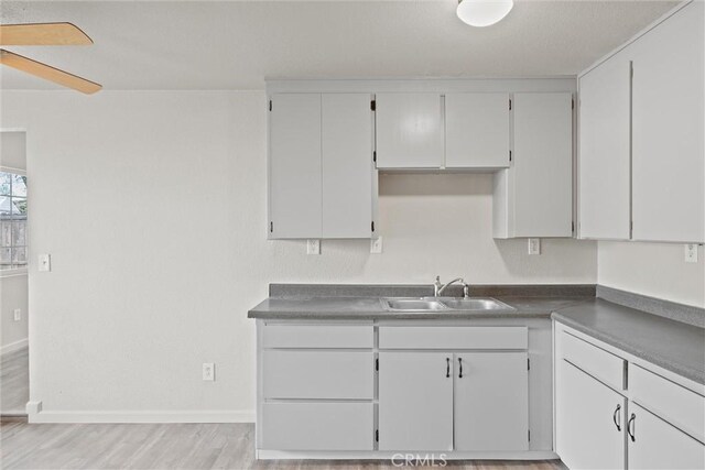 kitchen with baseboards, light wood-style flooring, white cabinetry, ceiling fan, and a sink