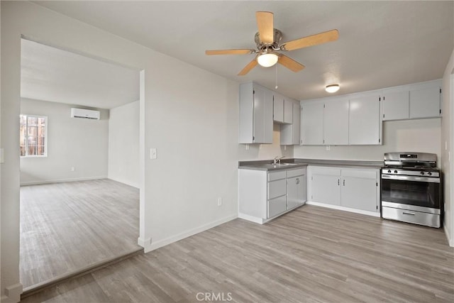 kitchen featuring an AC wall unit, baseboards, light wood-style floors, and stainless steel range with gas cooktop