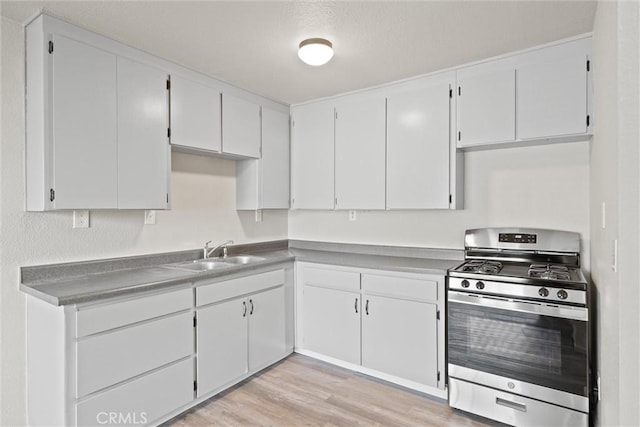 kitchen with light wood-type flooring, stainless steel gas range, white cabinetry, and a sink
