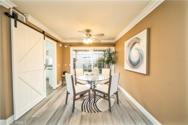 dining space featuring light wood-style flooring, ornamental molding, baseboards, and a barn door