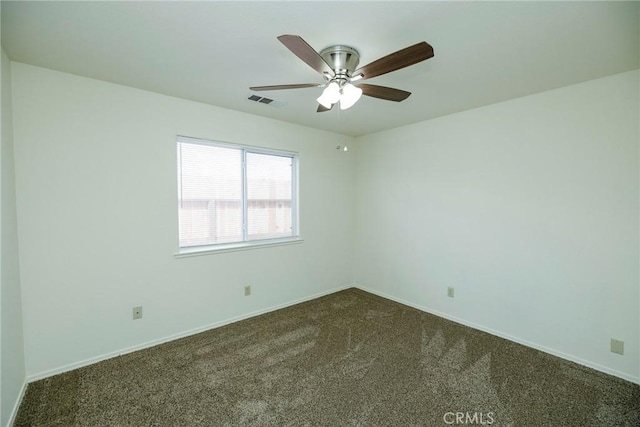 spare room featuring baseboards, dark colored carpet, a ceiling fan, and visible vents
