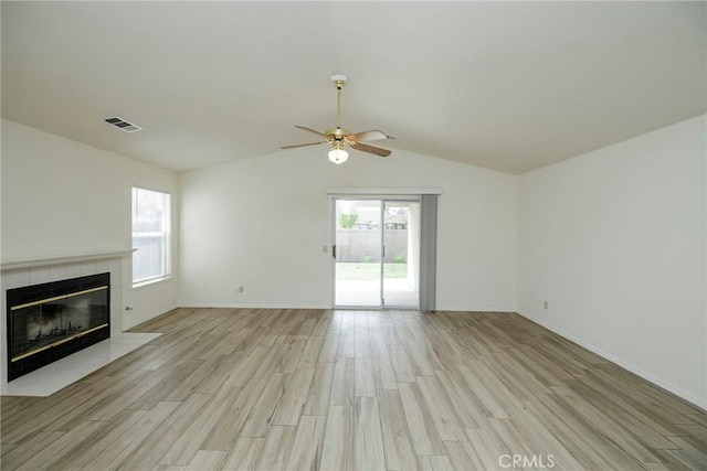 unfurnished living room featuring vaulted ceiling, plenty of natural light, a fireplace, light wood-style floors, and ceiling fan