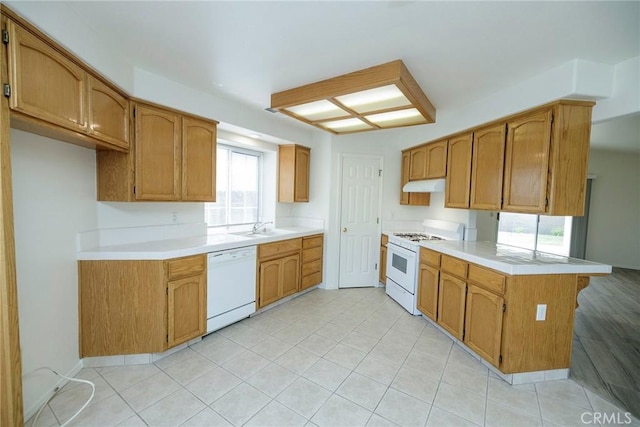kitchen featuring a sink, light countertops, white appliances, a peninsula, and under cabinet range hood