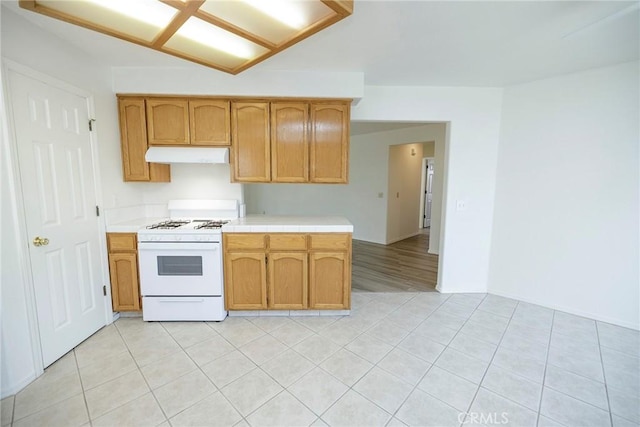 kitchen with white gas stove, light tile patterned floors, tile countertops, and under cabinet range hood