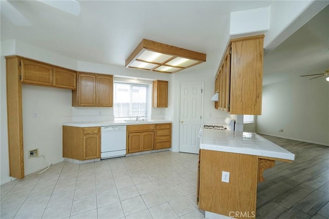 kitchen with white appliances, a peninsula, a ceiling fan, brown cabinetry, and a sink