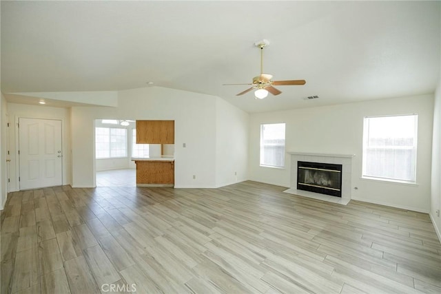 unfurnished living room featuring a fireplace, a ceiling fan, vaulted ceiling, visible vents, and light wood finished floors