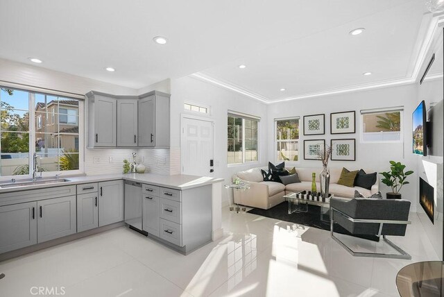 kitchen with gray cabinetry, open floor plan, a sink, stainless steel dishwasher, and light countertops