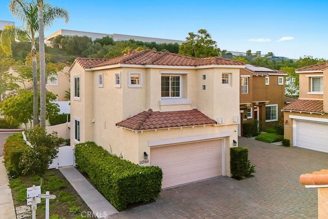 mediterranean / spanish-style home with a tiled roof, stucco siding, a garage, and decorative driveway