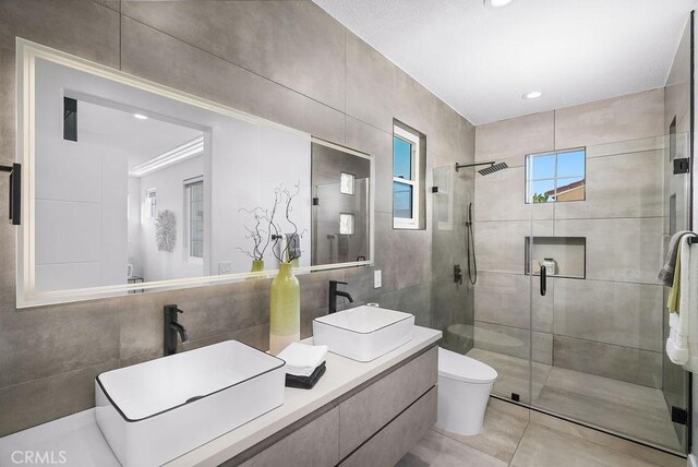 bathroom featuring tile walls, a shower stall, toilet, tile patterned flooring, and double vanity