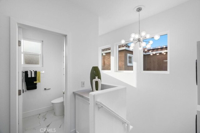 bathroom featuring marble finish flooring, toilet, baseboards, and a chandelier