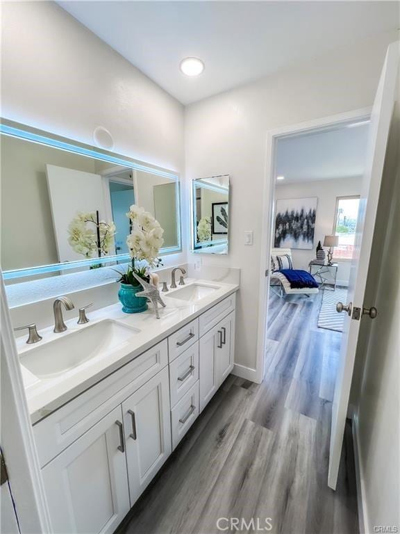 ensuite bathroom featuring wood finished floors, connected bathroom, double vanity, and a sink