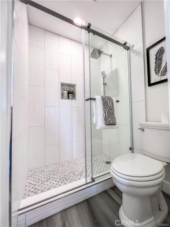 bathroom with a stall shower, toilet, and wood finished floors