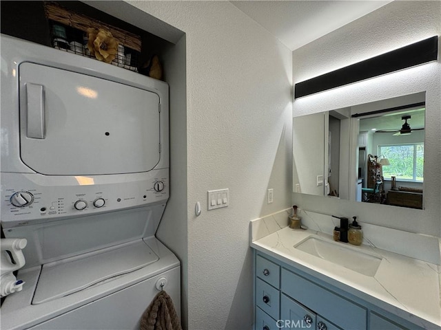 laundry area featuring a sink, a textured wall, ceiling fan, and stacked washer / drying machine
