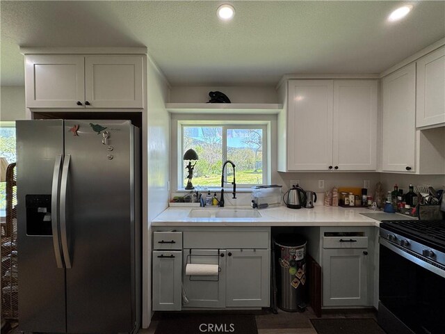 kitchen with gas range, a sink, white cabinetry, and stainless steel refrigerator with ice dispenser