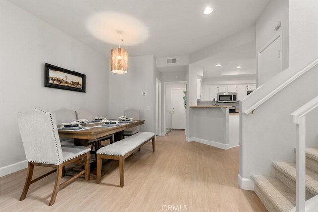 dining area with light wood-type flooring, visible vents, baseboards, and stairs