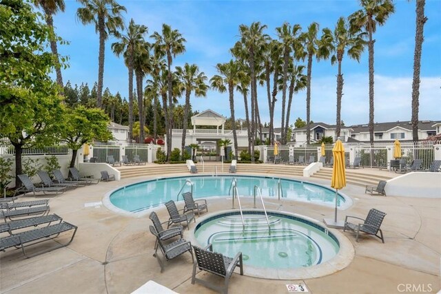 community pool featuring fence, a hot tub, a patio area, and a residential view