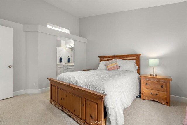 bedroom with ensuite bathroom, baseboards, and light colored carpet