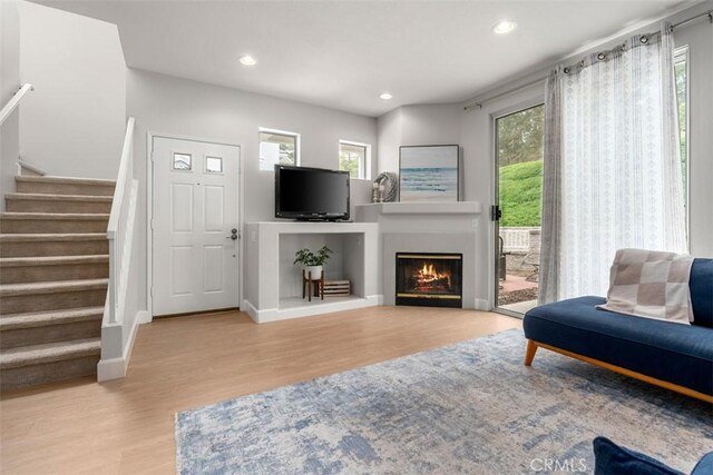 living room featuring recessed lighting, wood finished floors, stairs, and a lit fireplace