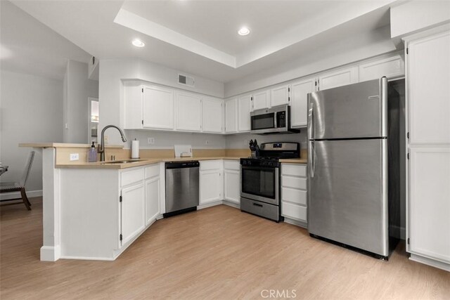 kitchen featuring light wood finished floors, a peninsula, a sink, recessed lighting, and appliances with stainless steel finishes