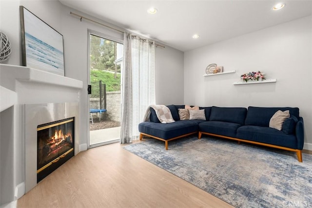 living room with recessed lighting, a glass covered fireplace, and wood finished floors